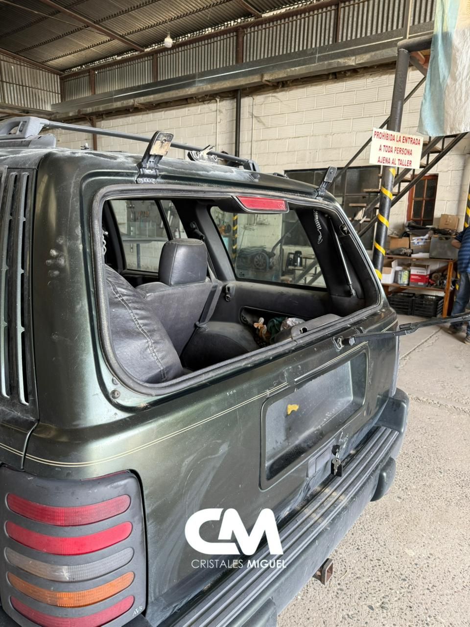 Vista trasera de un todoterreno verde oscuro con la ventana trasera rota, estacionado dentro de un garaje.