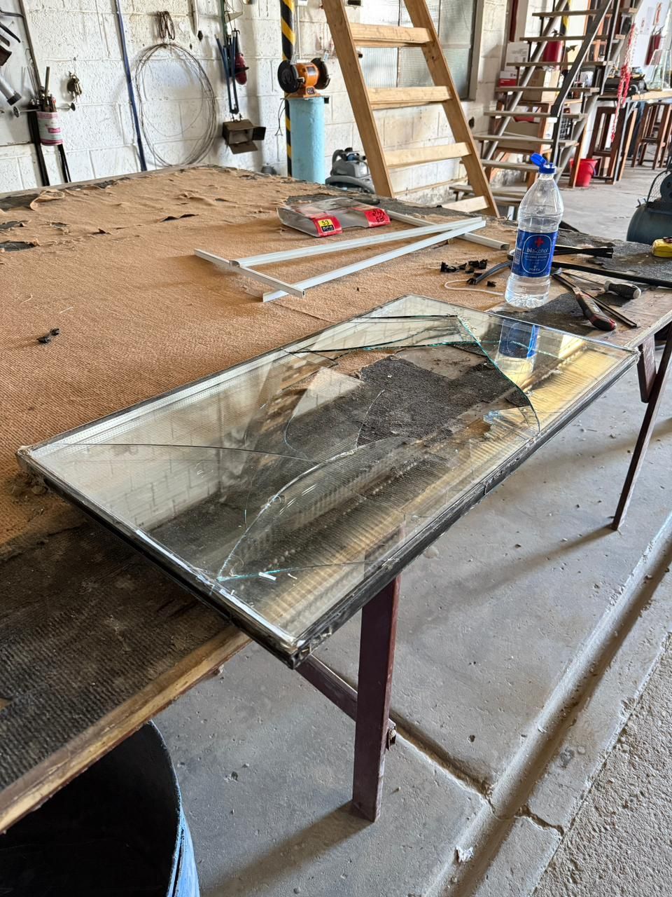 Espejo roto sobre una mesa de madera, herramientas de construcción en un taller.