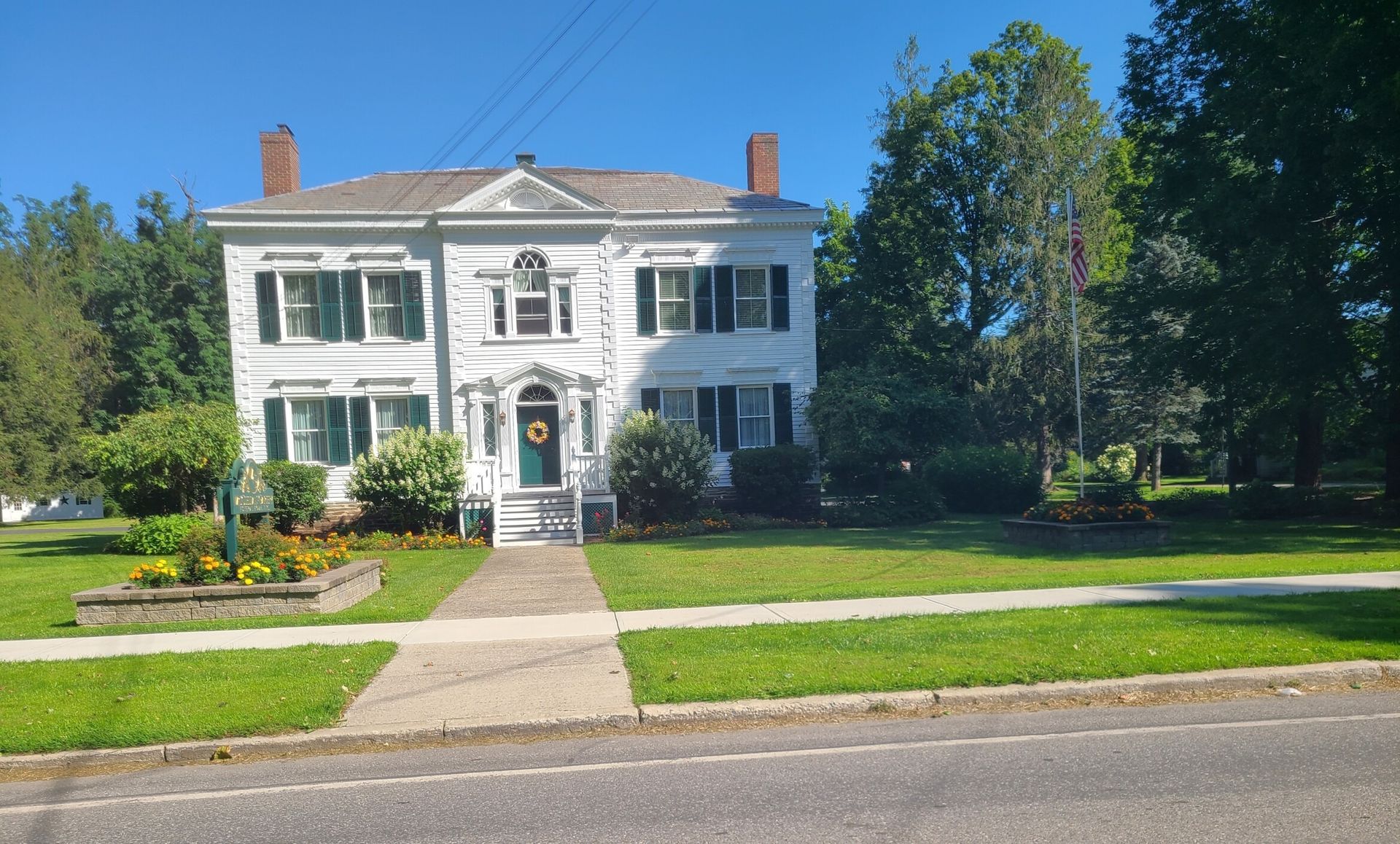 White two-story colonial house with columns, front lawn, garden, and trees on a sunny day