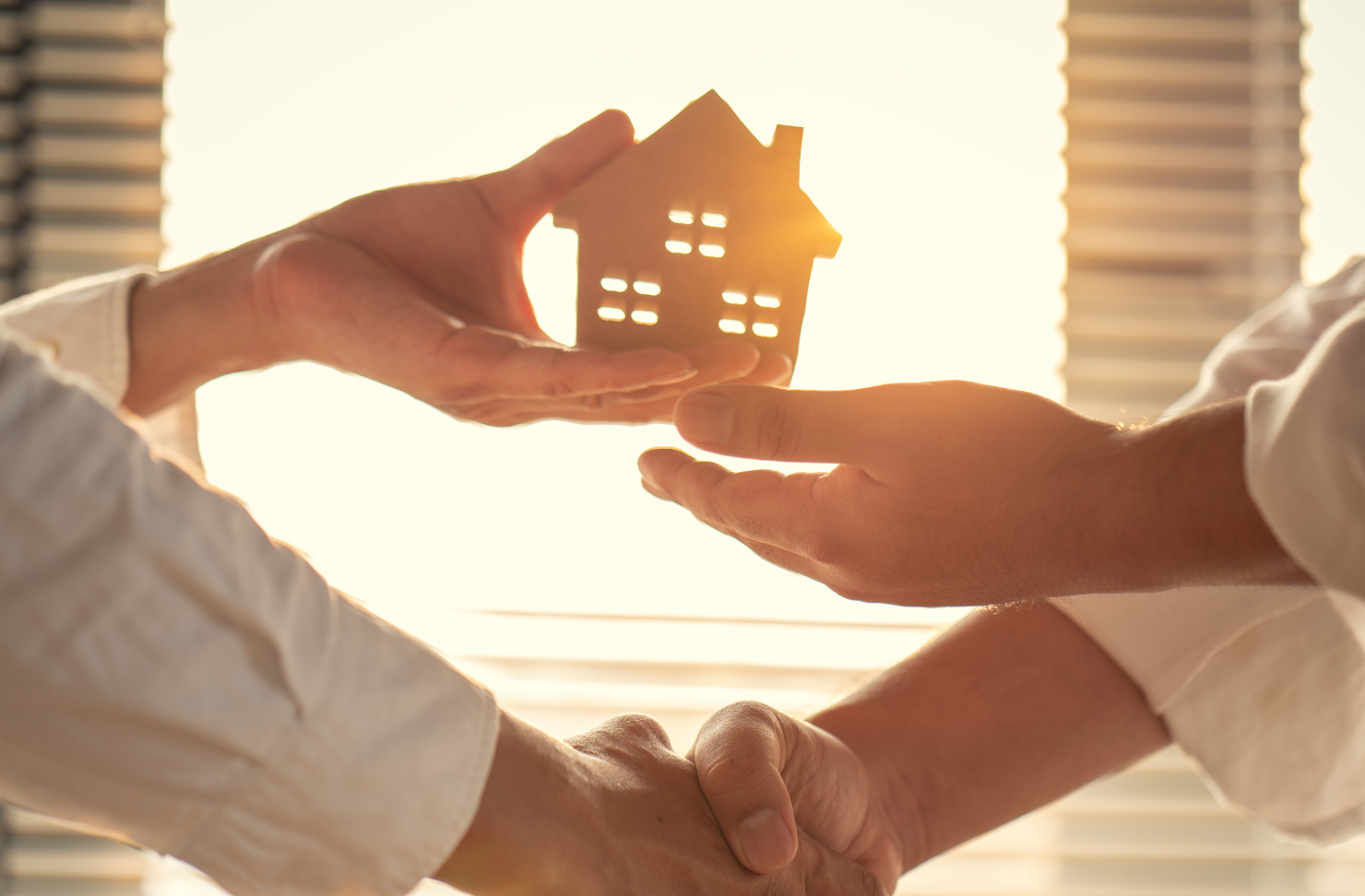 A man is shaking hands with another man while holding a model house.