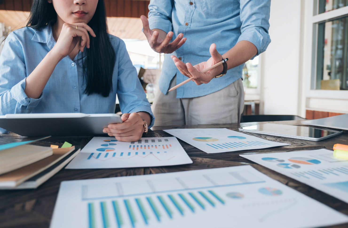 A man and a woman are sitting at a table with papers and a tablet.