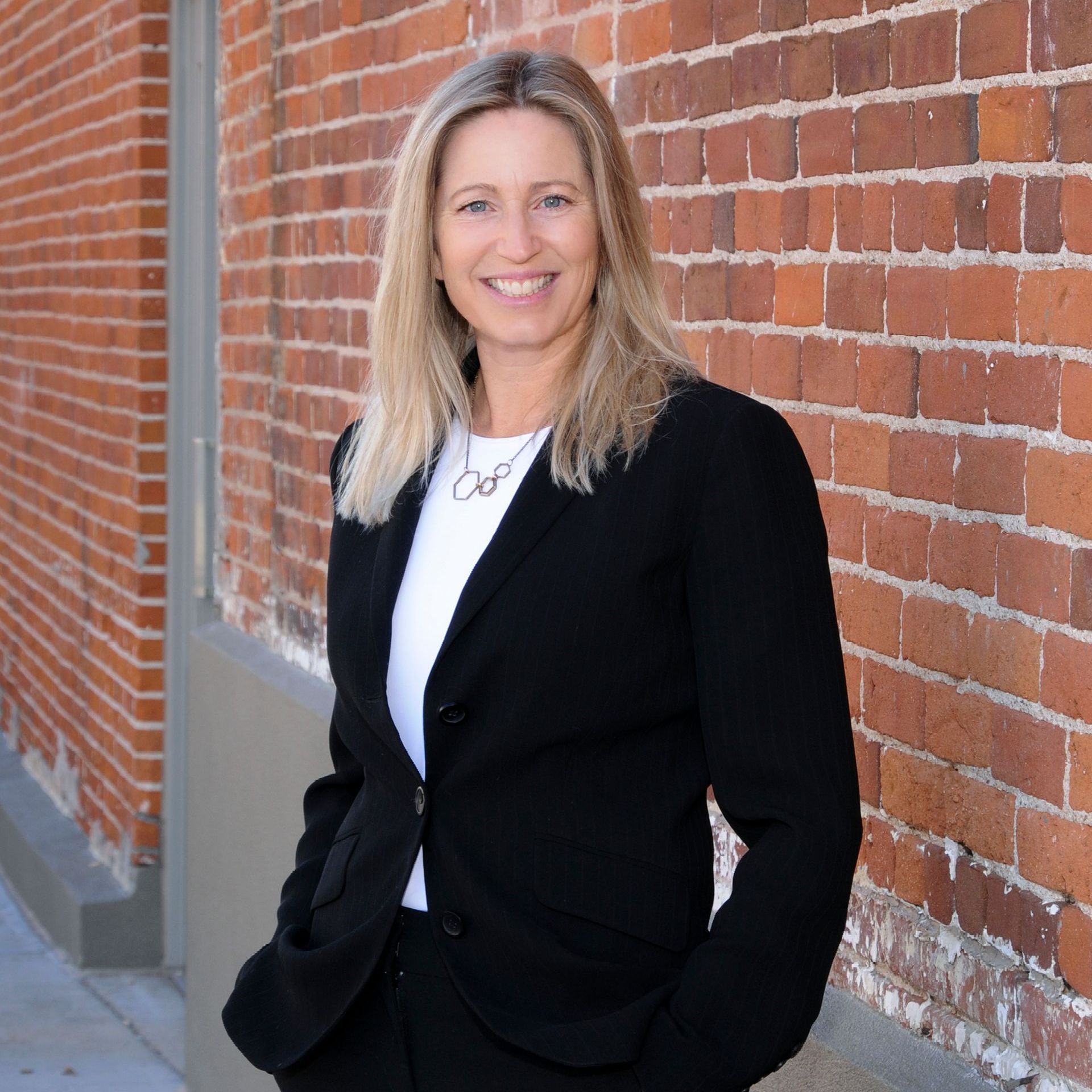 A woman in a black jacket is standing in front of a brick wall