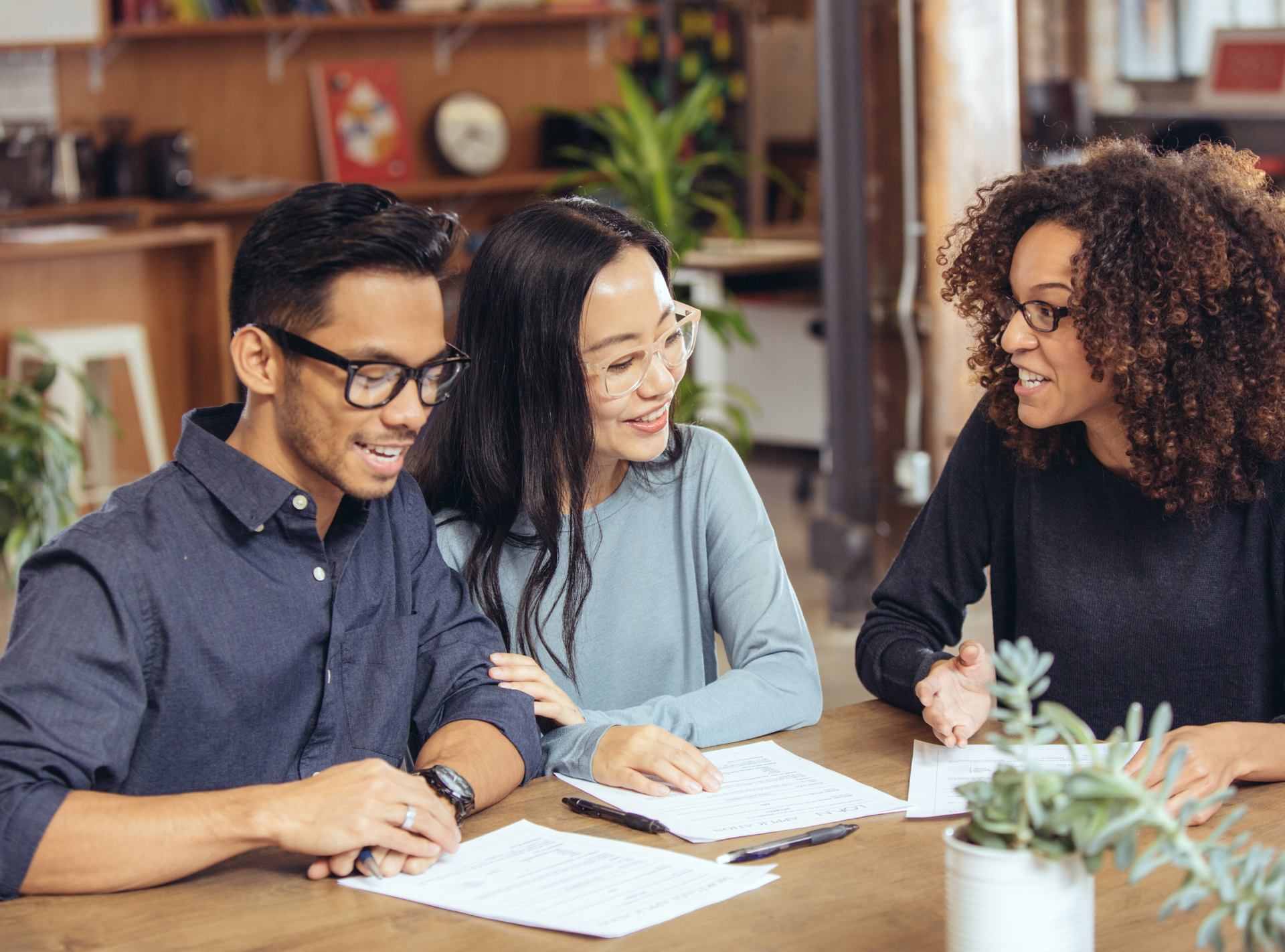 A man and two women are sitting at a table looking at papers.