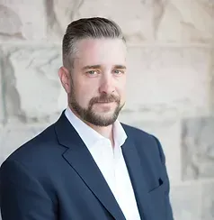 A man with a beard is wearing a suit and white shirt.