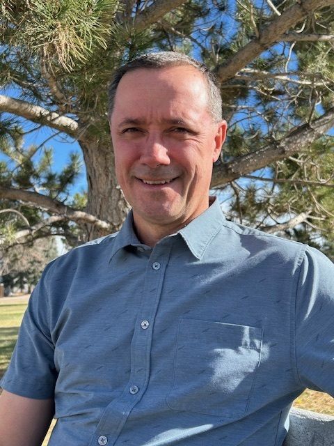 A man in a blue shirt is sitting in front of a tree.