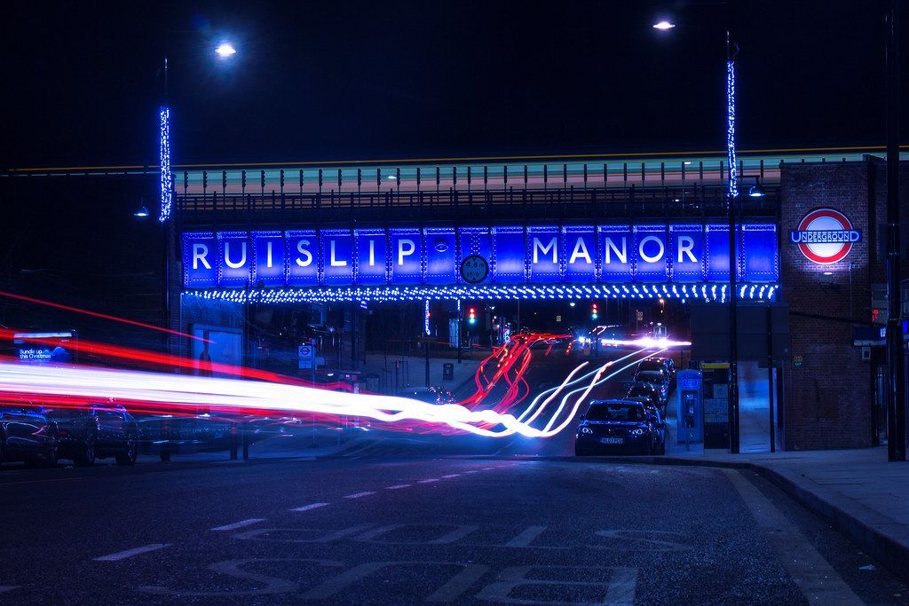 Group of diverse students and teachers taking a selfie outside; some smiling, wearing red and black shirts, near a building.