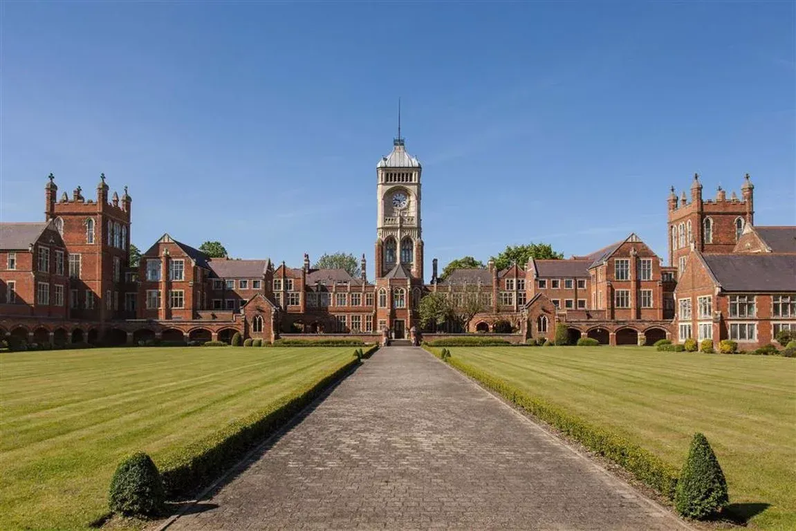 Brick building with central tower, flanked by symmetrical wings, grass lawn, and path on a sunny day.