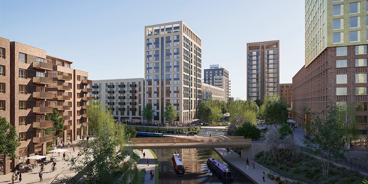 Cityscape of modern brick buildings along a canal with trees and a pedestrian bridge.