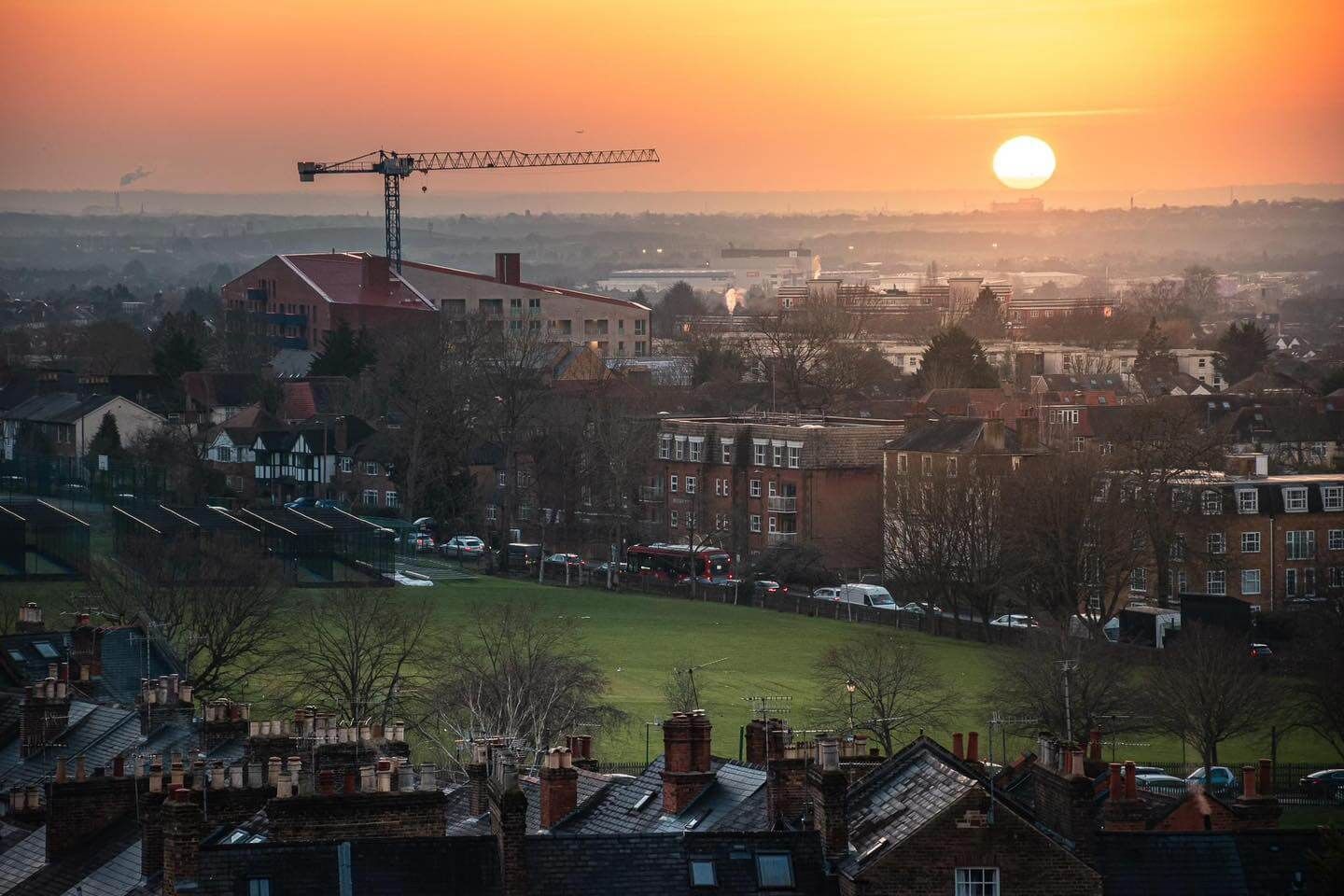 Sunset over a cityscape, with a construction crane silhouetted. Warm light and orange sky.