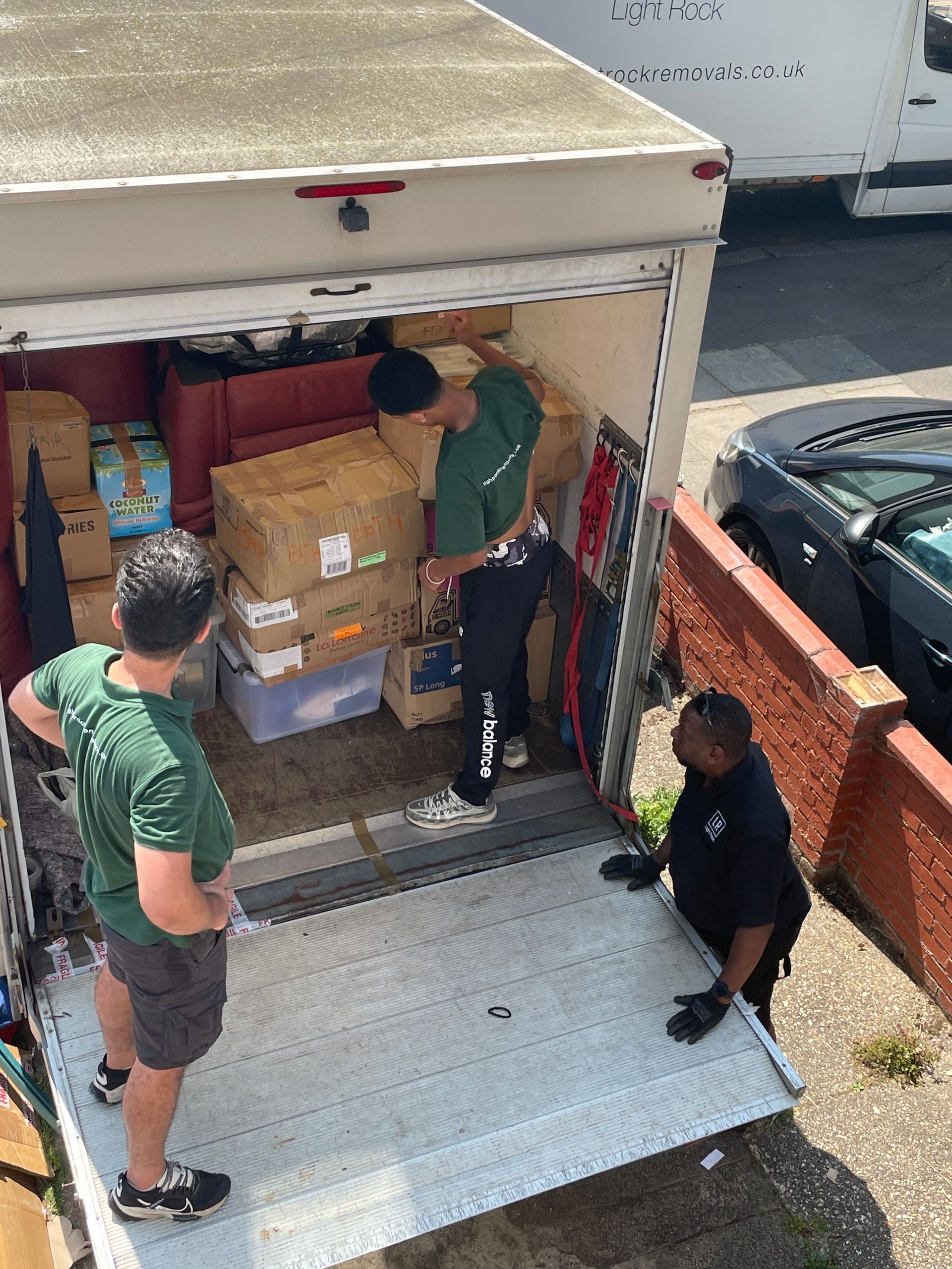 Movers loading a truck with boxes and furniture on a sunny day.