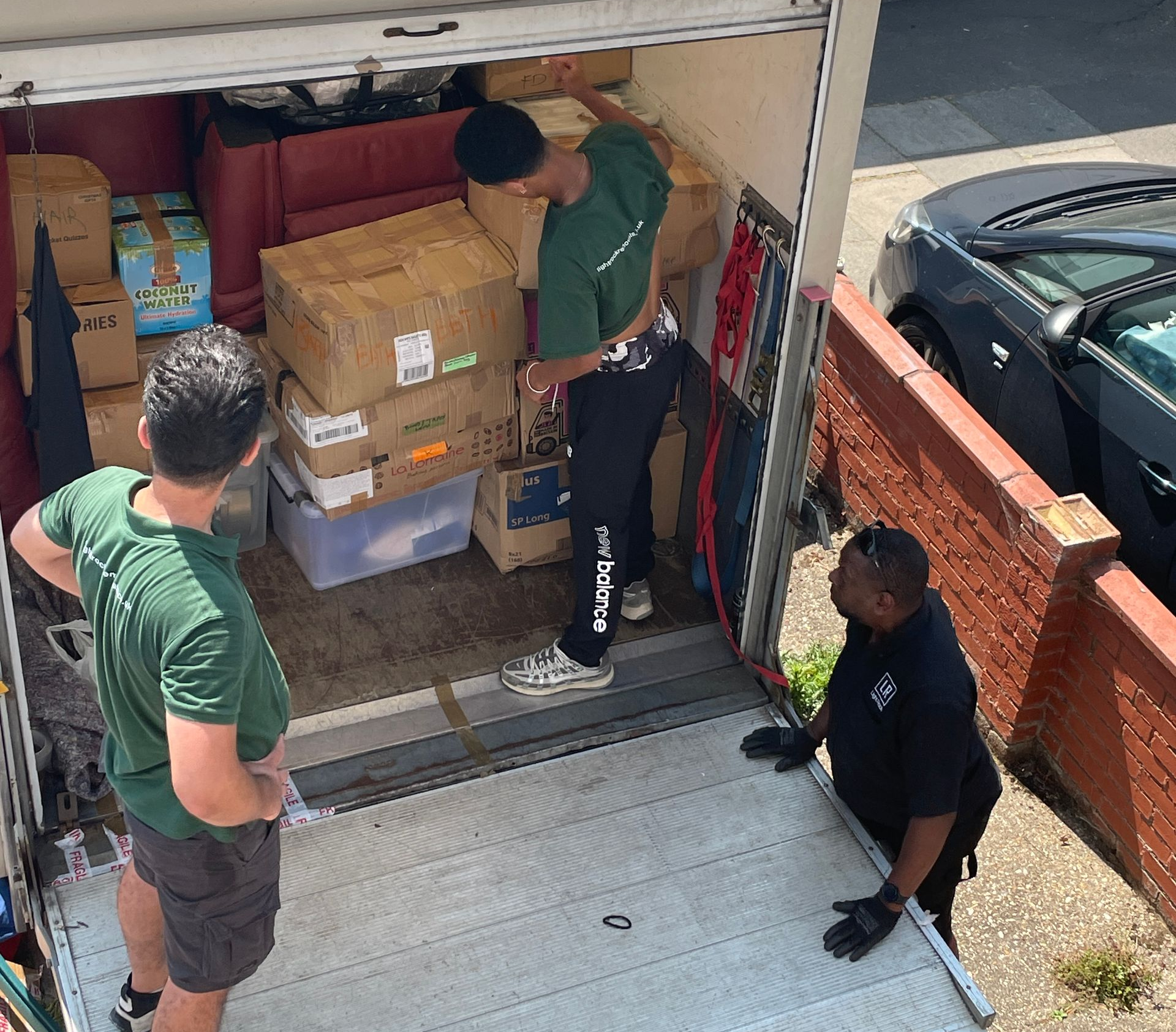 Three people loading boxes into a moving truck. One person is in the truck, two are outside.