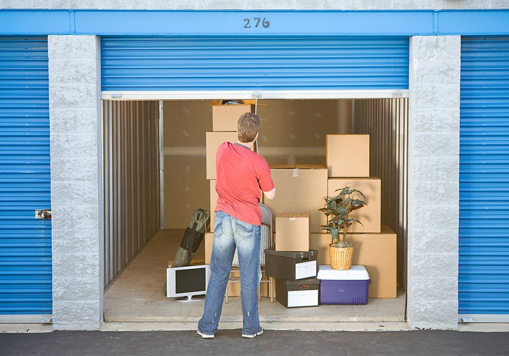A person looks into an open blue storage unit filled with boxes, a TV, and other items.