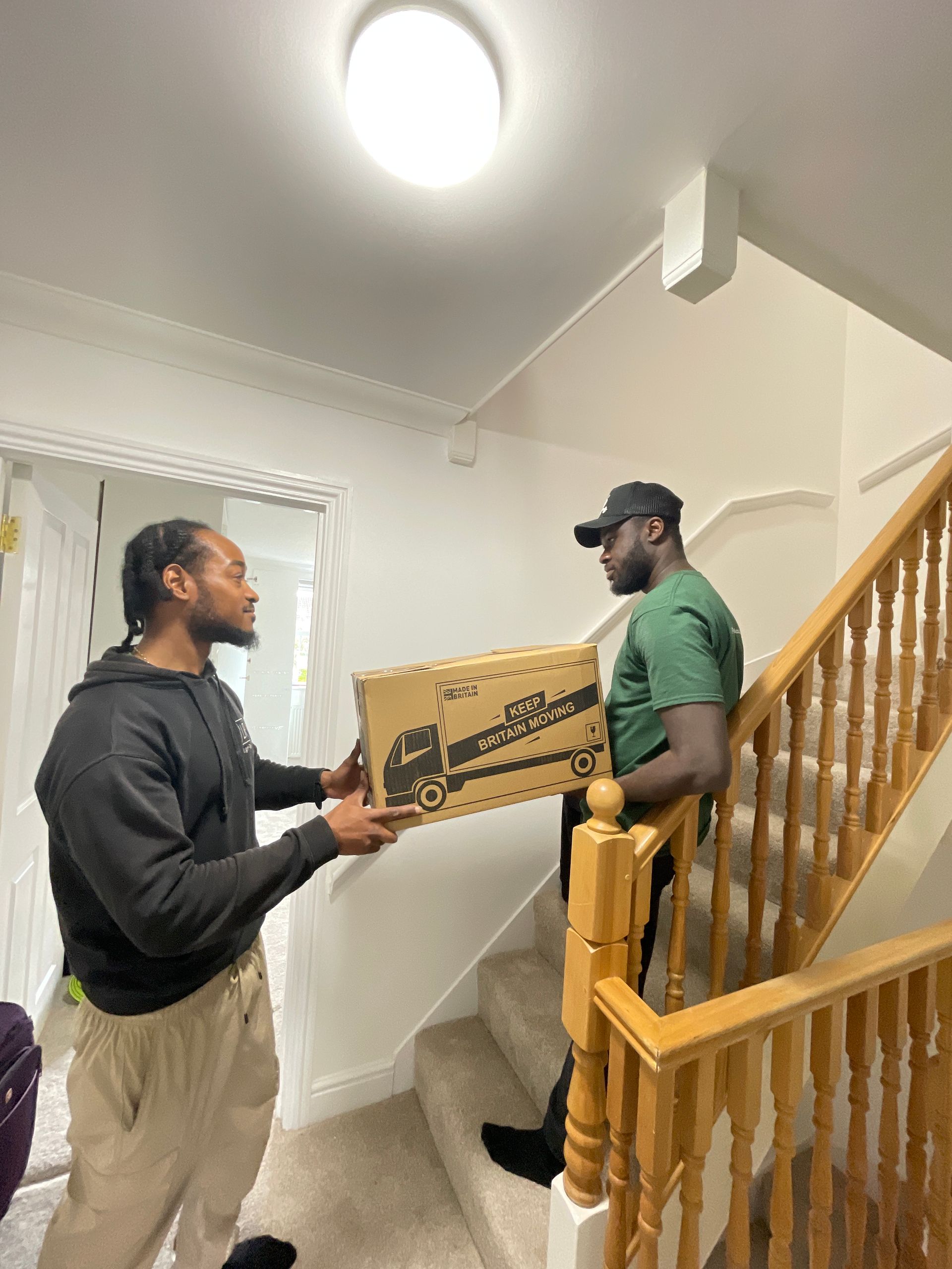 Two men on stairs, one passing a cardboard box printed with a truck logo.