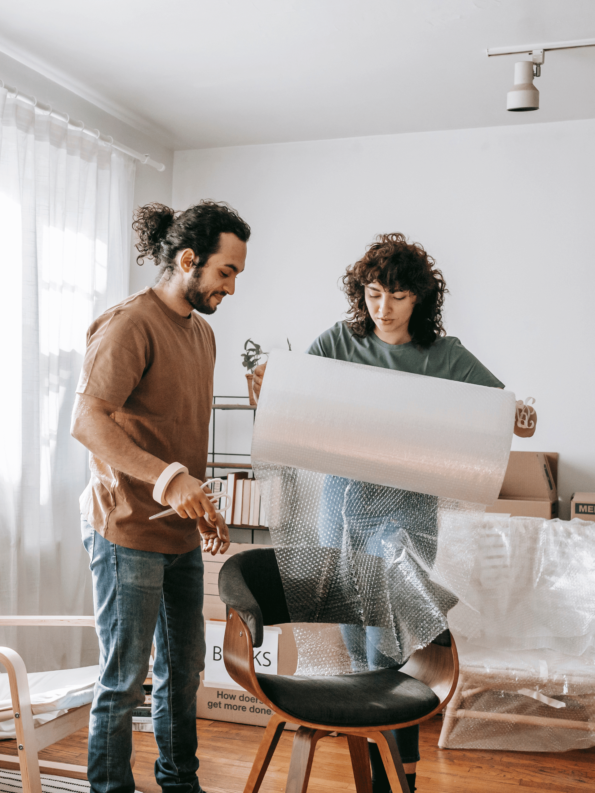 A man and a woman are wrapping a chair in plastic.