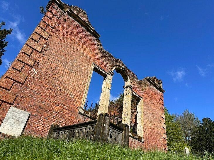 Ruins of a red brick building with arched windows against a clear blue sky.