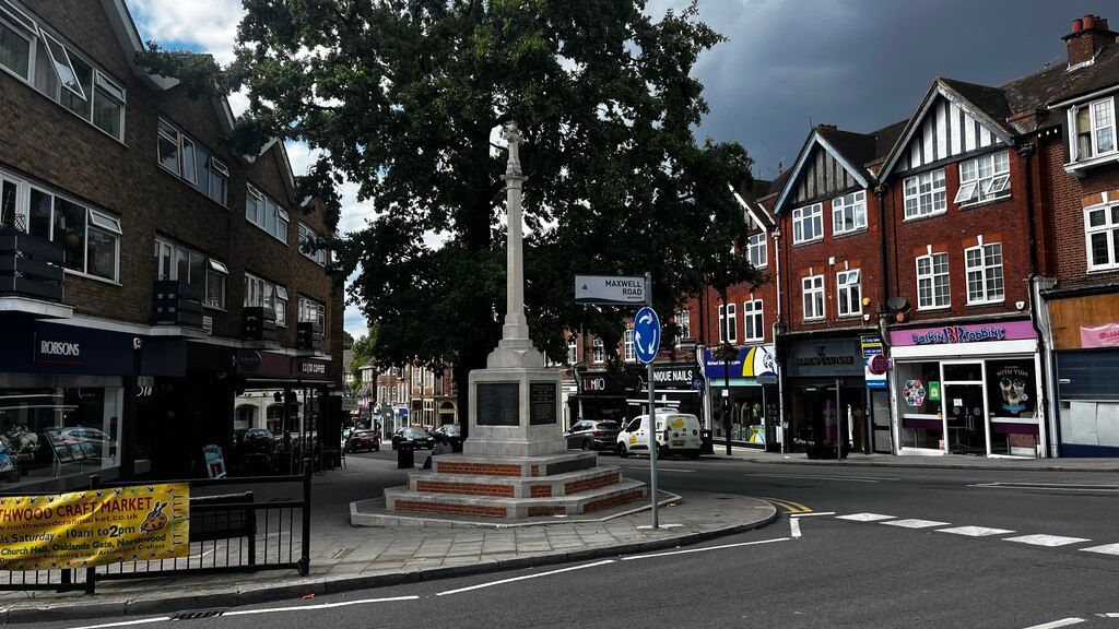 Stone cottages line a river in a Cotswold village, a small bridge in the foreground reflecting the colorful sunset sky.