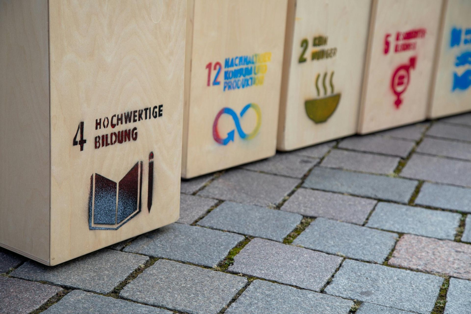 Wooden boxes displaying UN Sustainable Development Goals, standing on a cobblestone path.