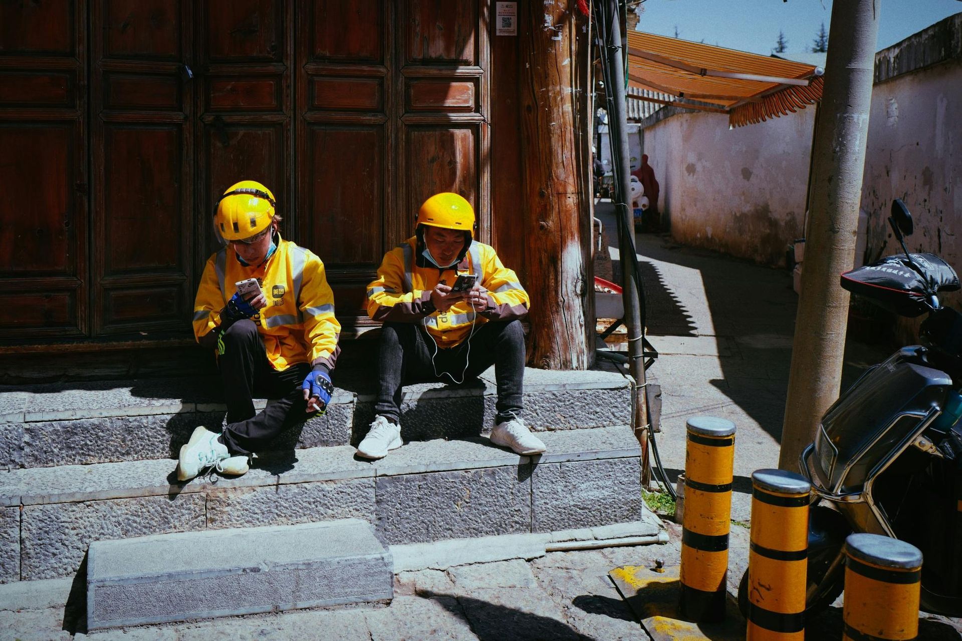 Two food delivery workers in yellow uniforms rest on steps.