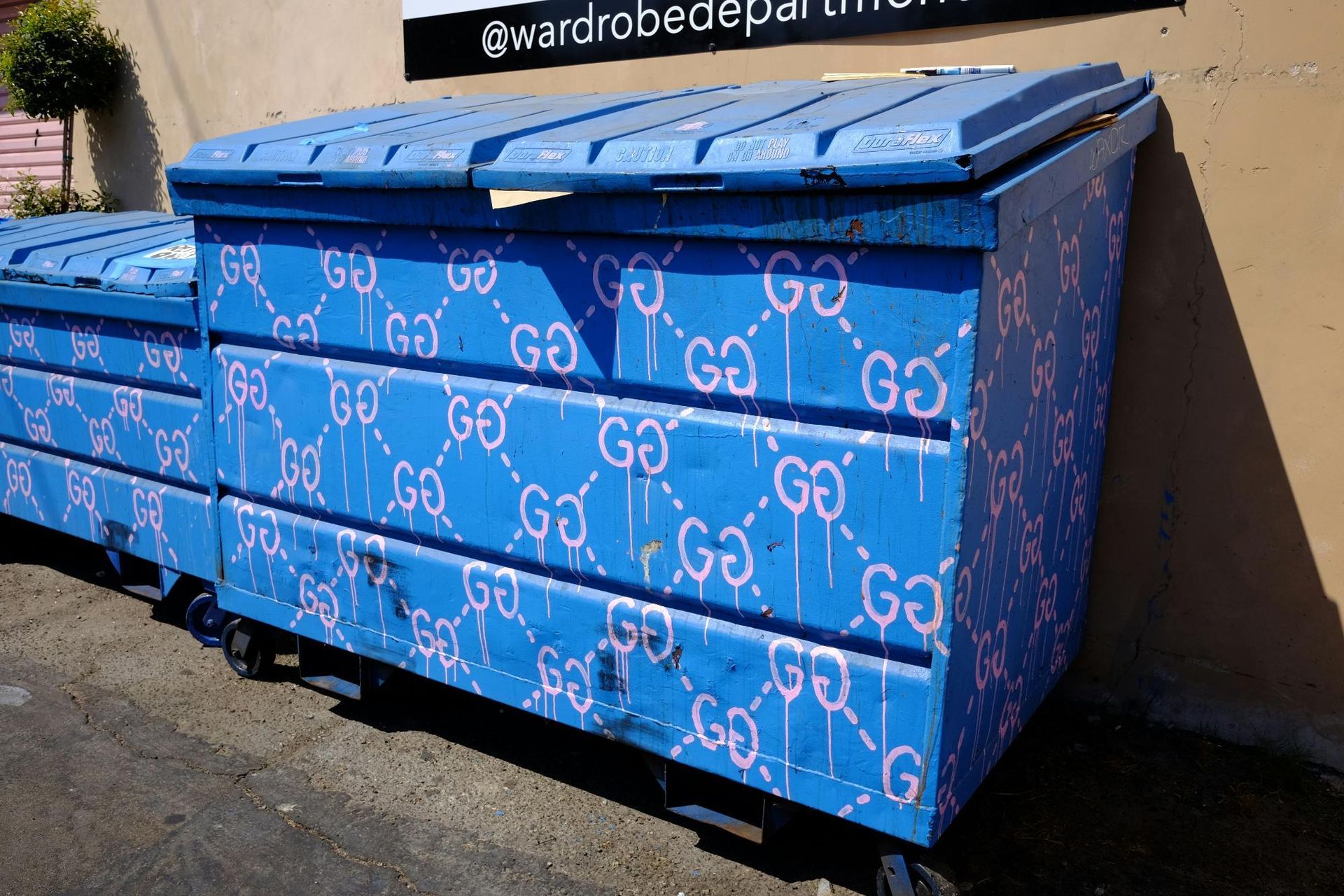 Blue dumpsters with graffiti-style Gucci logo pattern.
