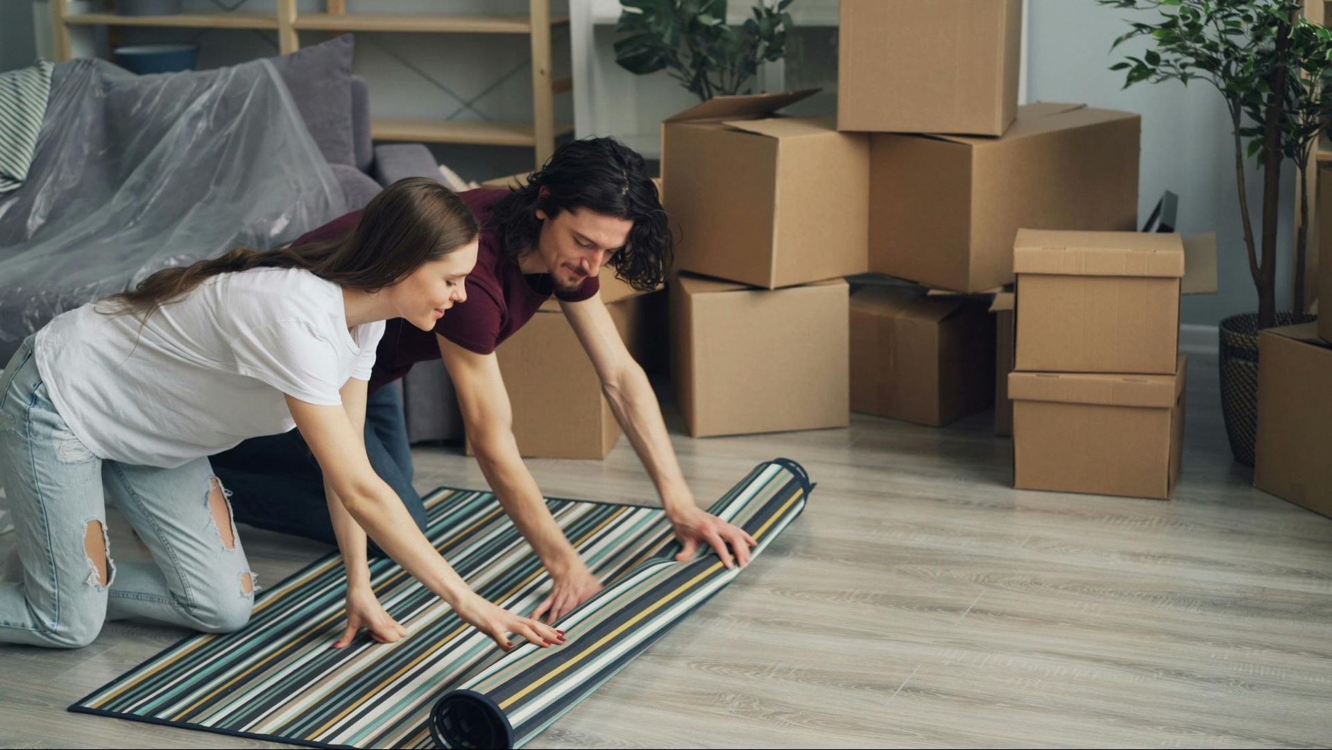 Couple unrolling a striped rug in a room with moving boxes.