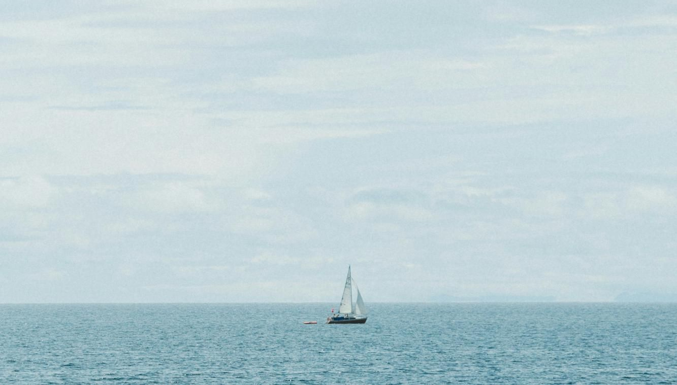 Sailboat on calm blue water under a cloudy sky.