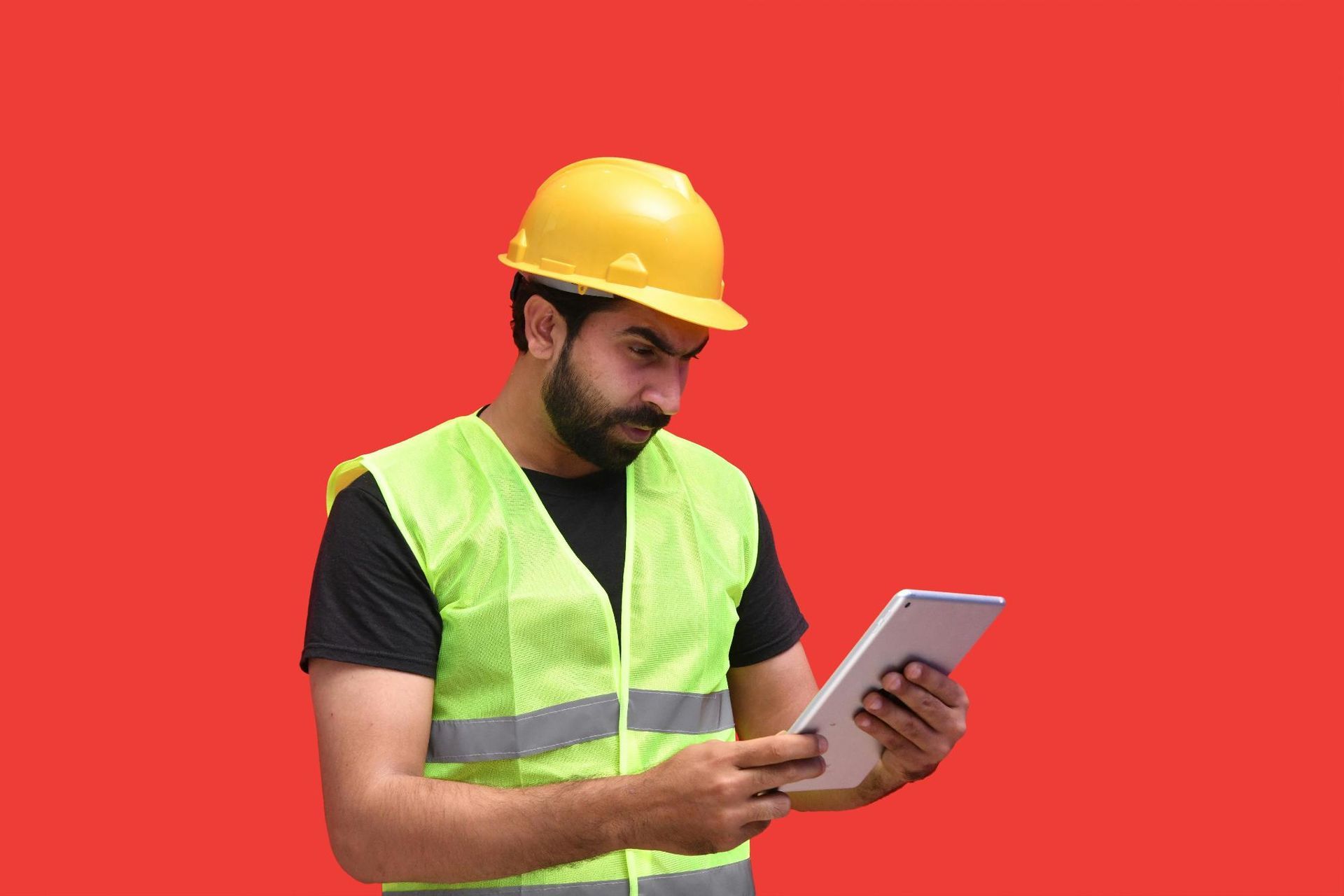 Construction worker wearing a hard hat and safety vest, looking at a tablet against a red background.