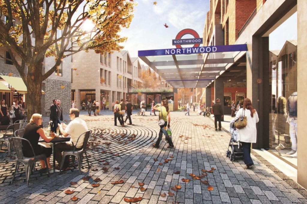 Two people feed deer carrots through a fence in a wooded area. The deer have large antlers.