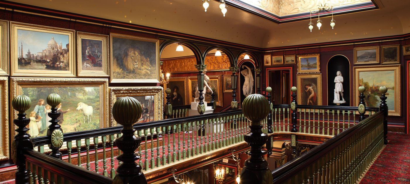 Two people feed deer carrots through a fence in a wooded area. The deer have large antlers.