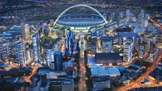An aerial view of Wembley Stadium at dusk, surrounded by buildings and lit streets.