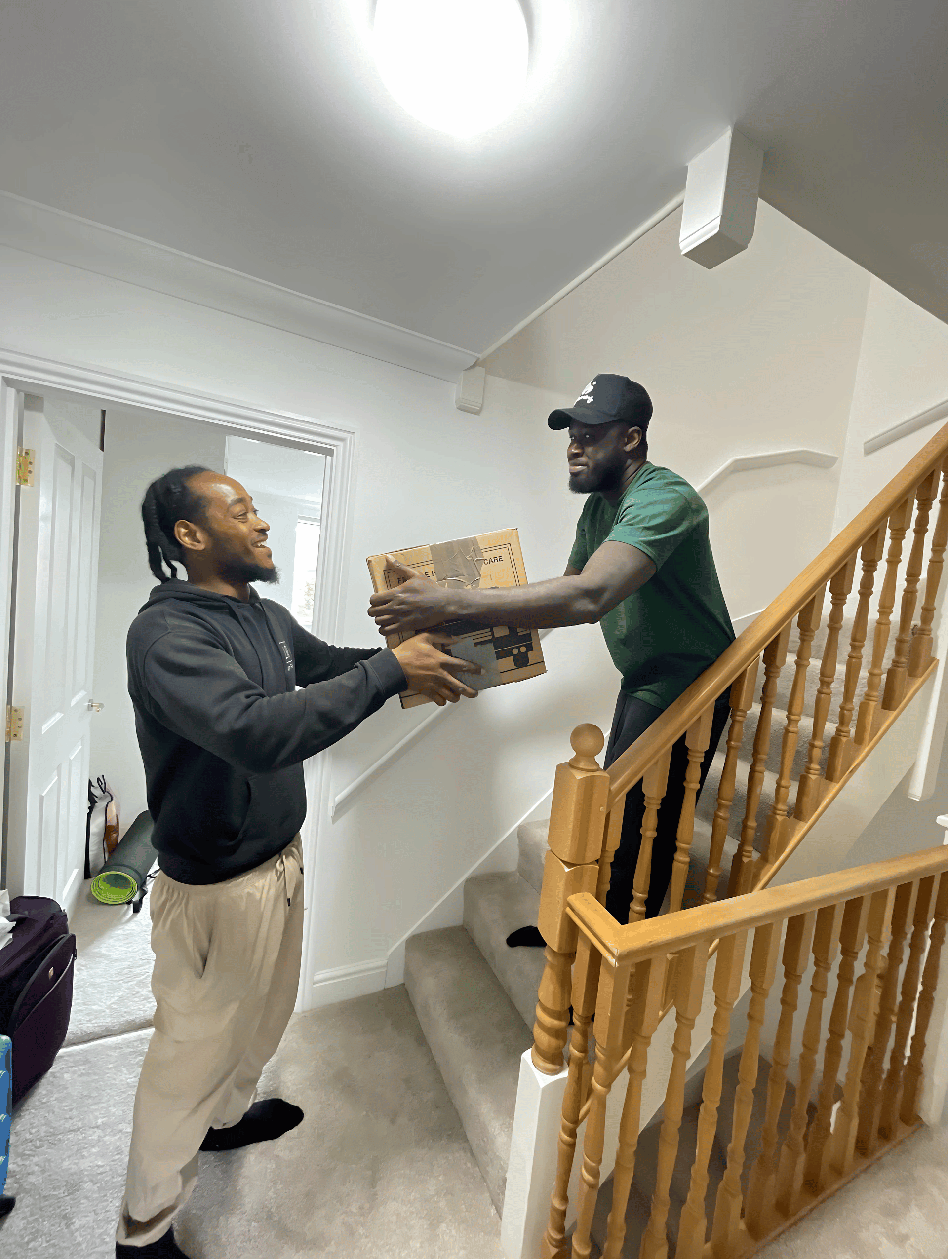 Two men passing a box on a staircase. One on the stairs, the other at the bottom.
