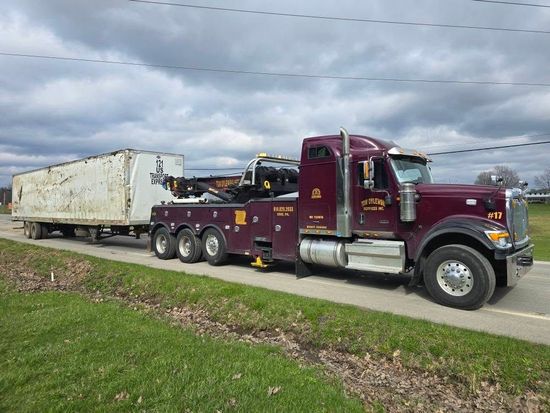 A red tow truck is towing a tractor in a field