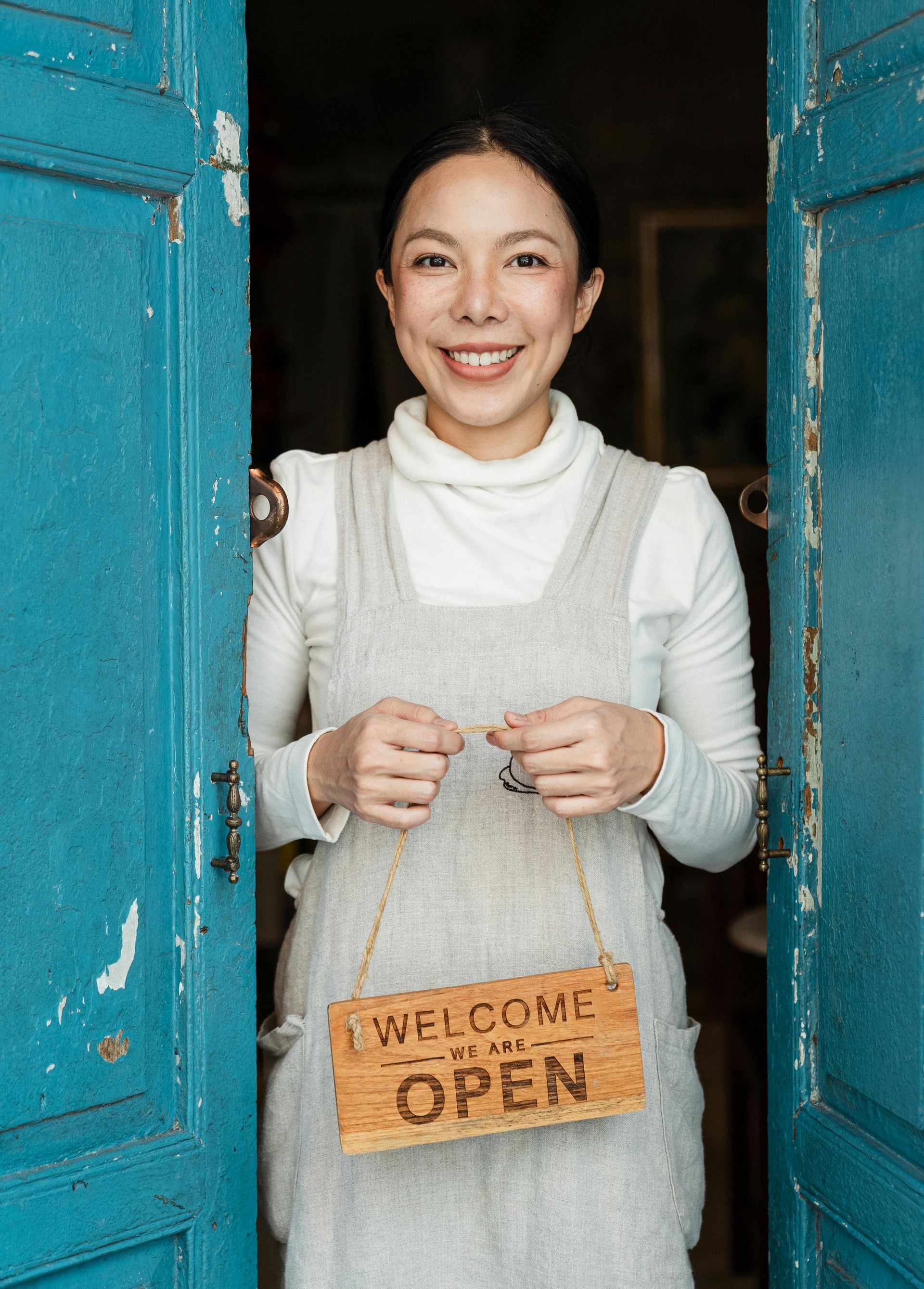 A man in an apron is standing in a restaurant with his arms crossed and smiling.