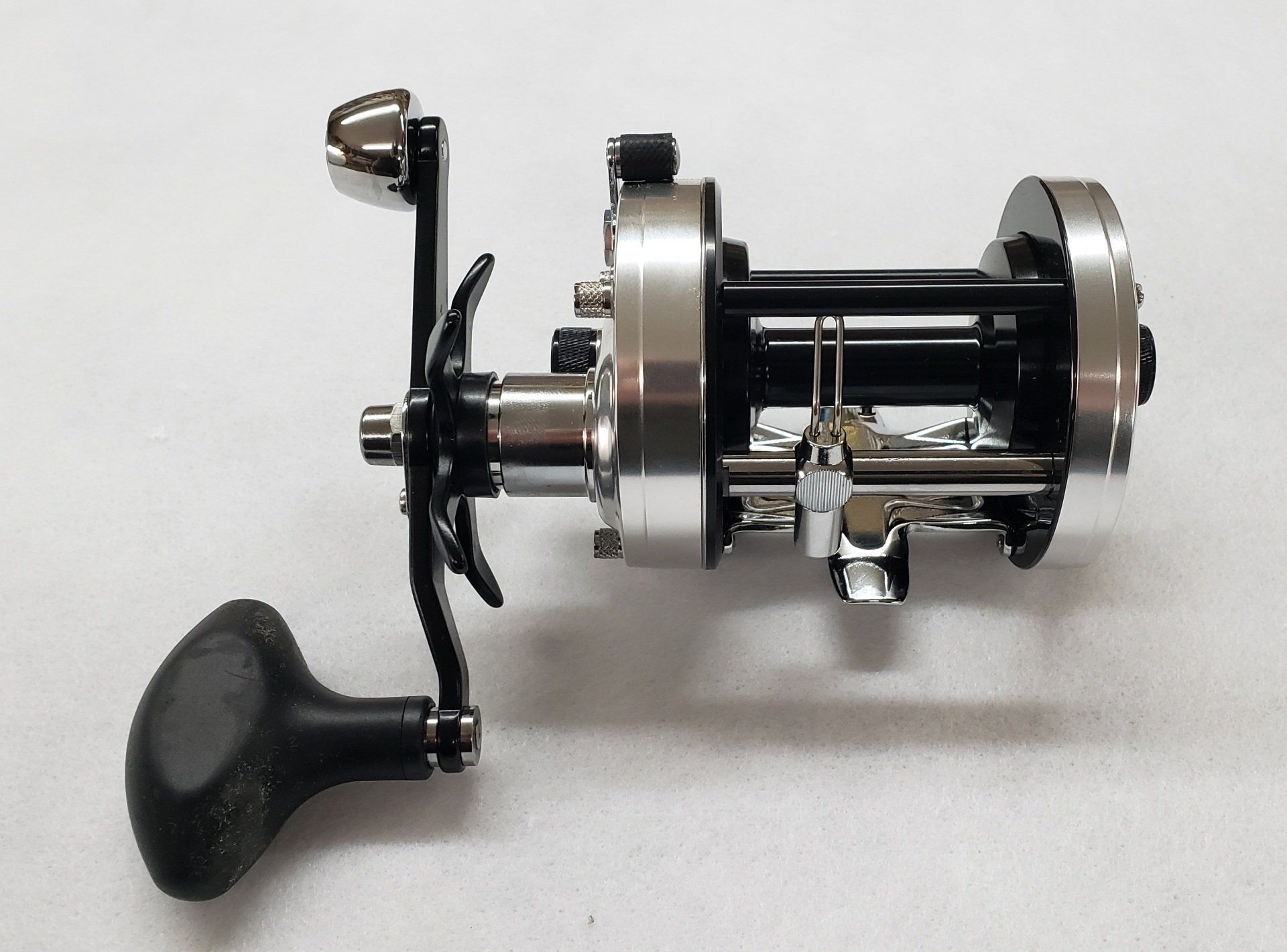 Black and silver fishing reel, side view, on white surface.