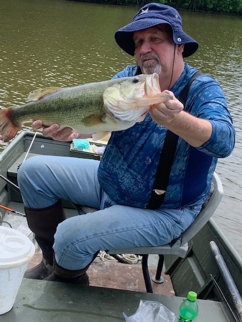 Man in a boat holding a large fish, wearing a blue shirt and hat, with water in the background.