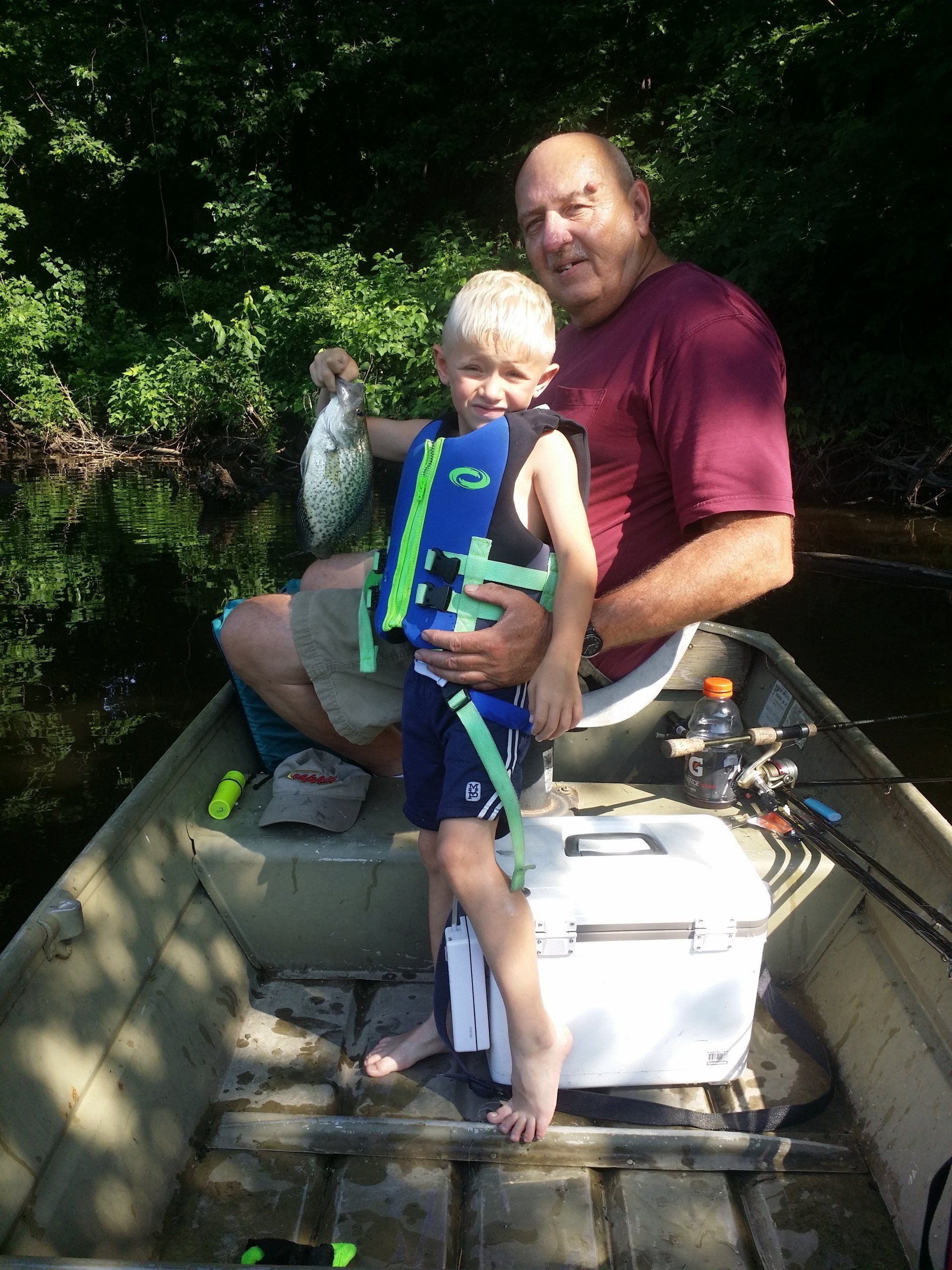 Man and child fishing in a boat, child holding a fish. They are smiling.