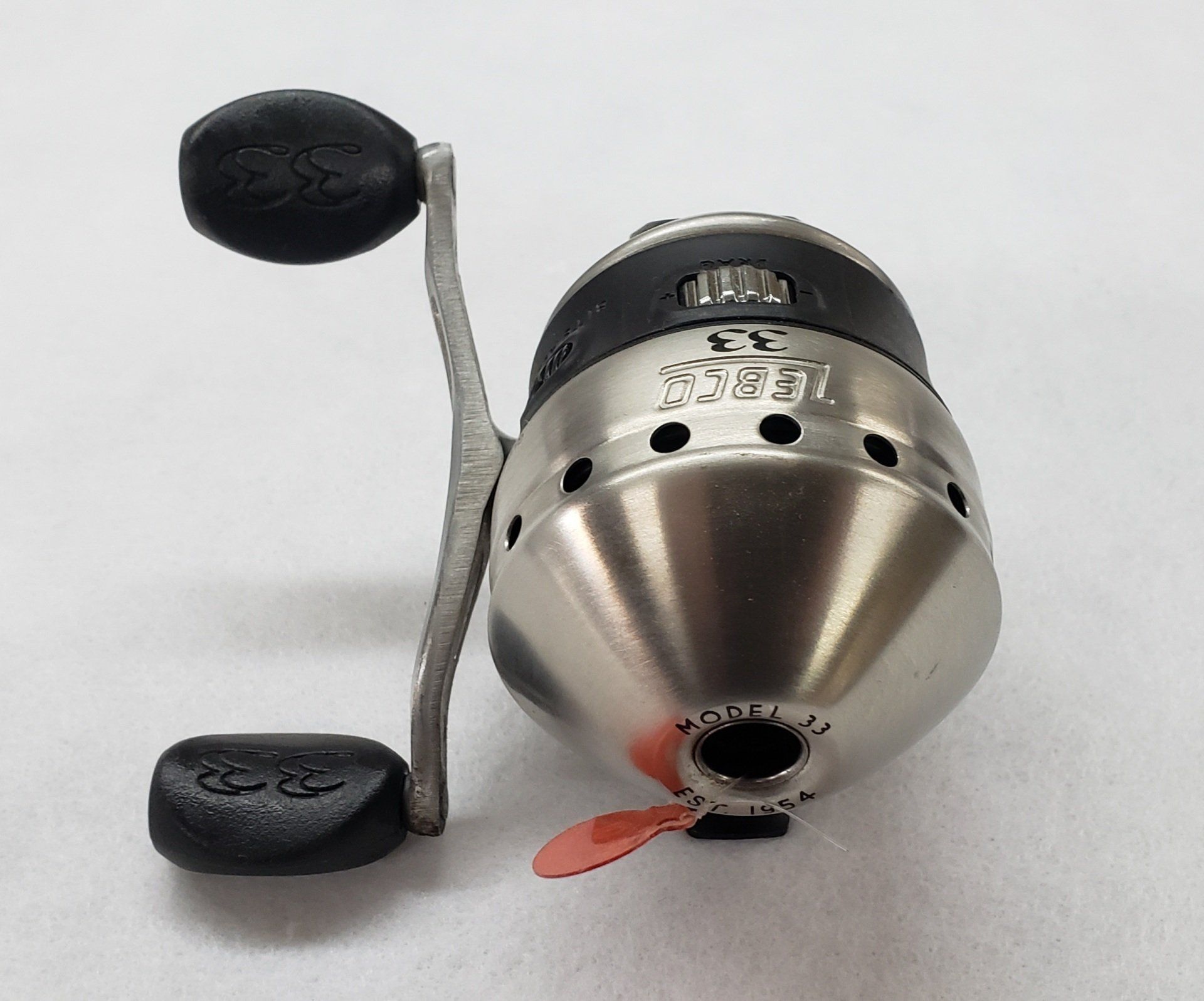 Silver and black fishing reel with handle, on a white surface.