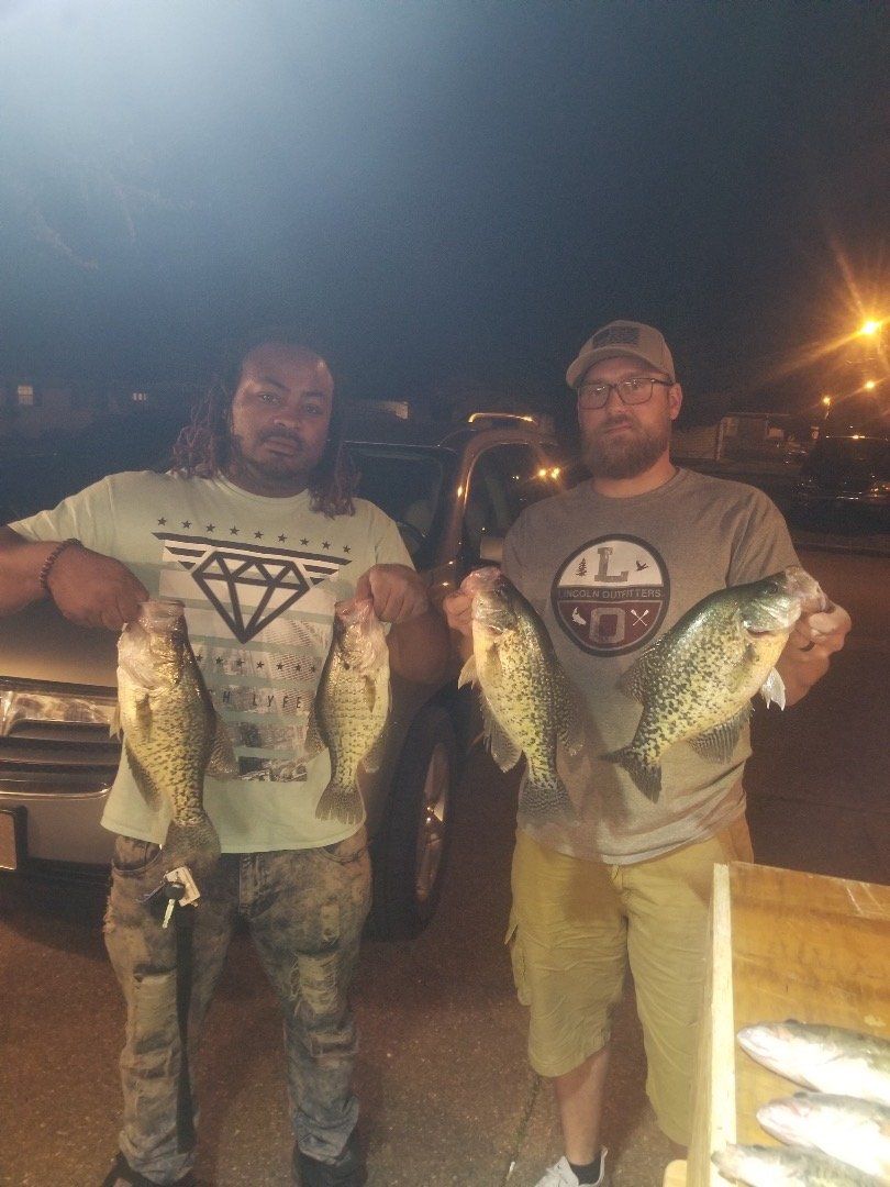 Two people holding up freshly caught fish at night.