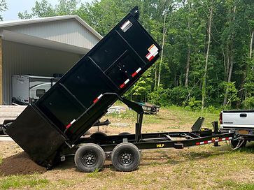 A dump trailer is parked in a grassy field next to a truck.