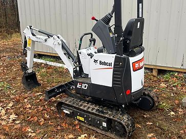 A small bobcat excavator is parked in front of a shed.