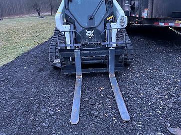 A bulldozer with forks attached to it is parked on a gravel road.