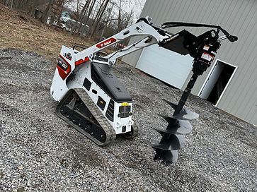 A bulldozer with a drill attached to it is sitting on a gravel road.