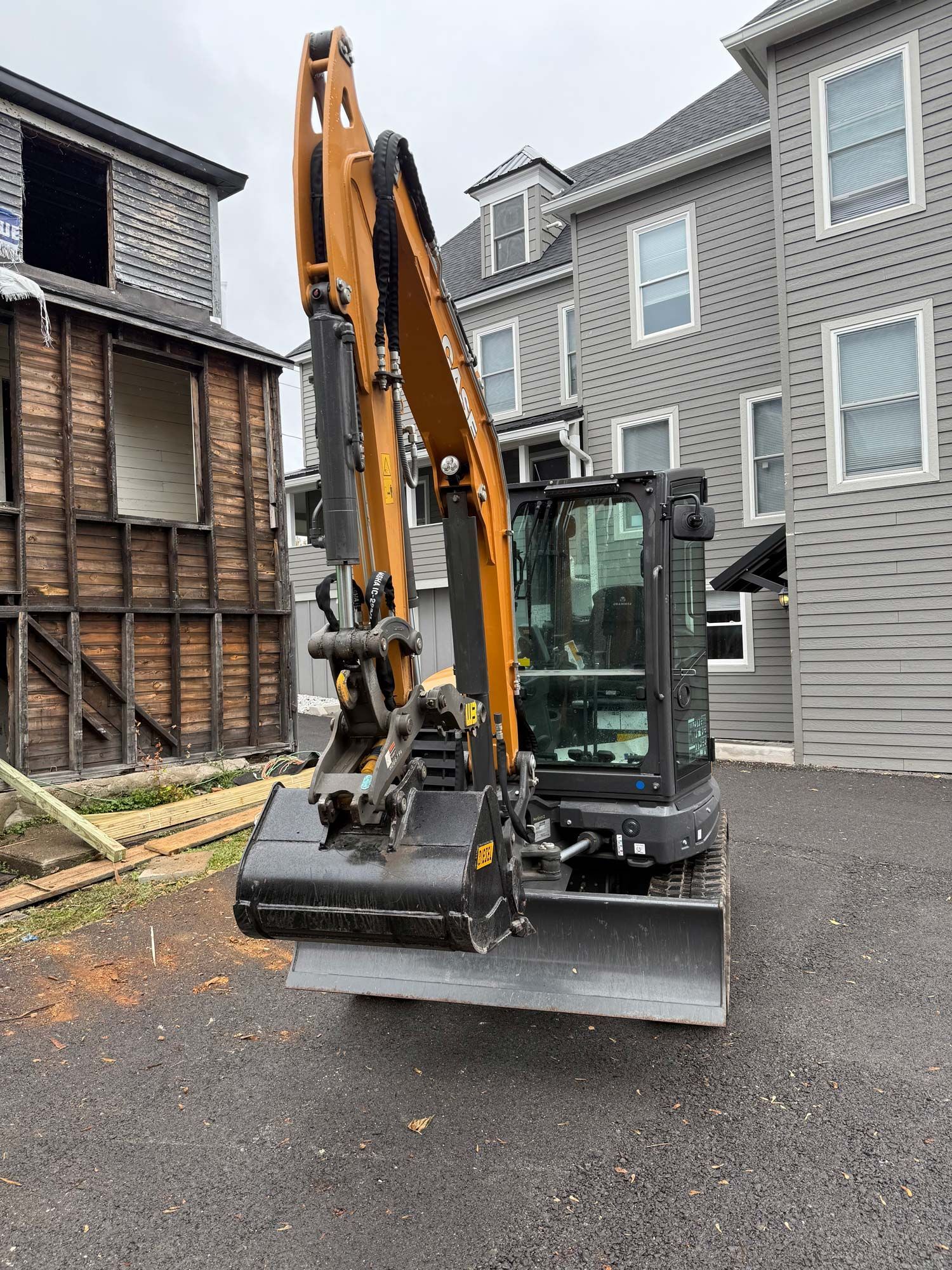 An excavator on a construction site. Brown and black machine, near a partially demolished building, gray sky.