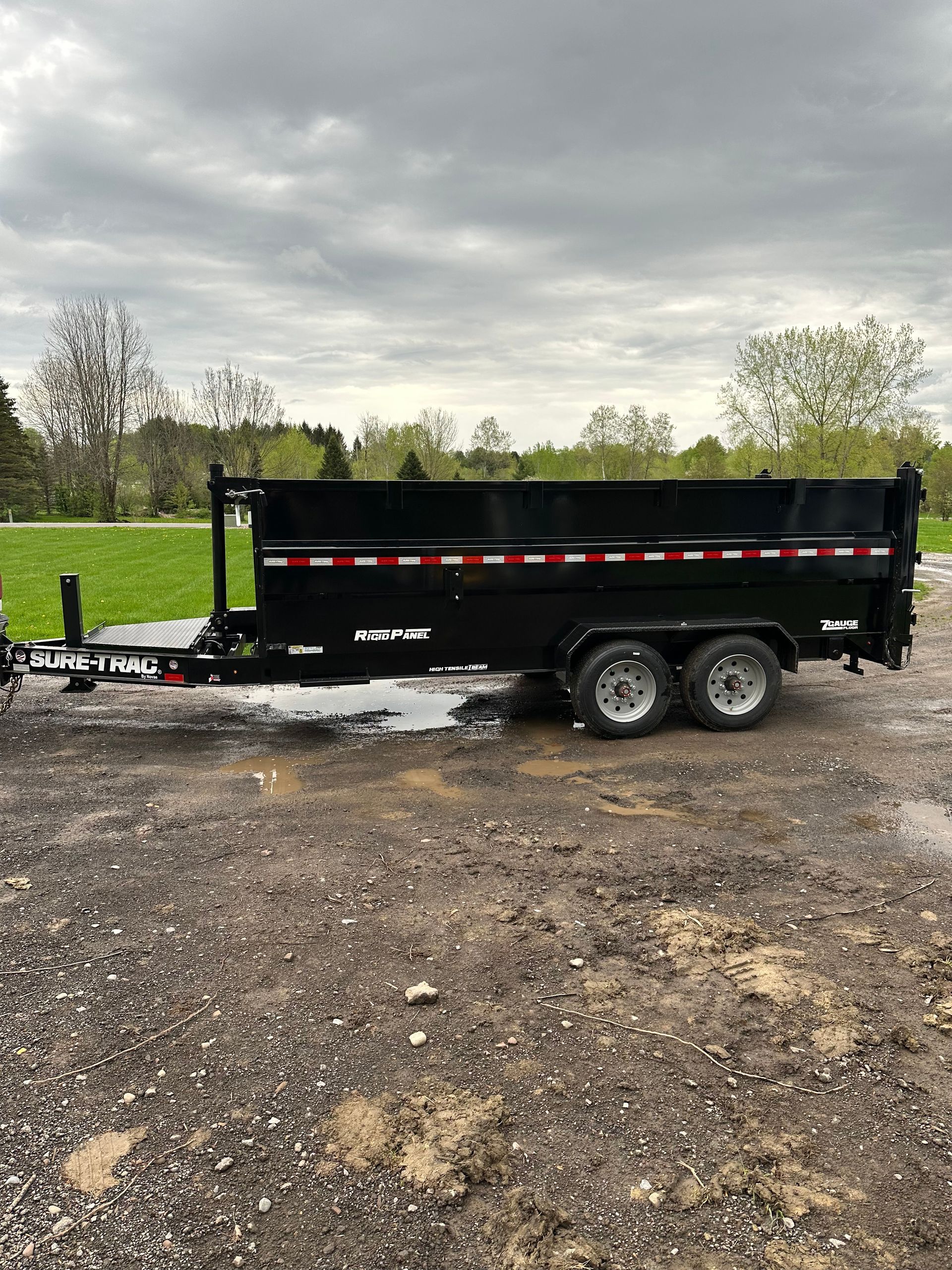 A dump trailer is parked in a gravel lot.
