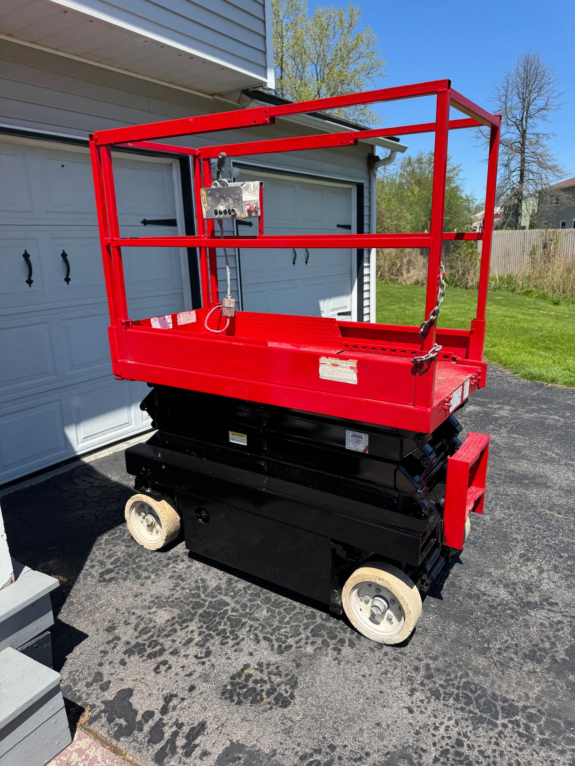 A red scissor lift is parked in front of a garage.
