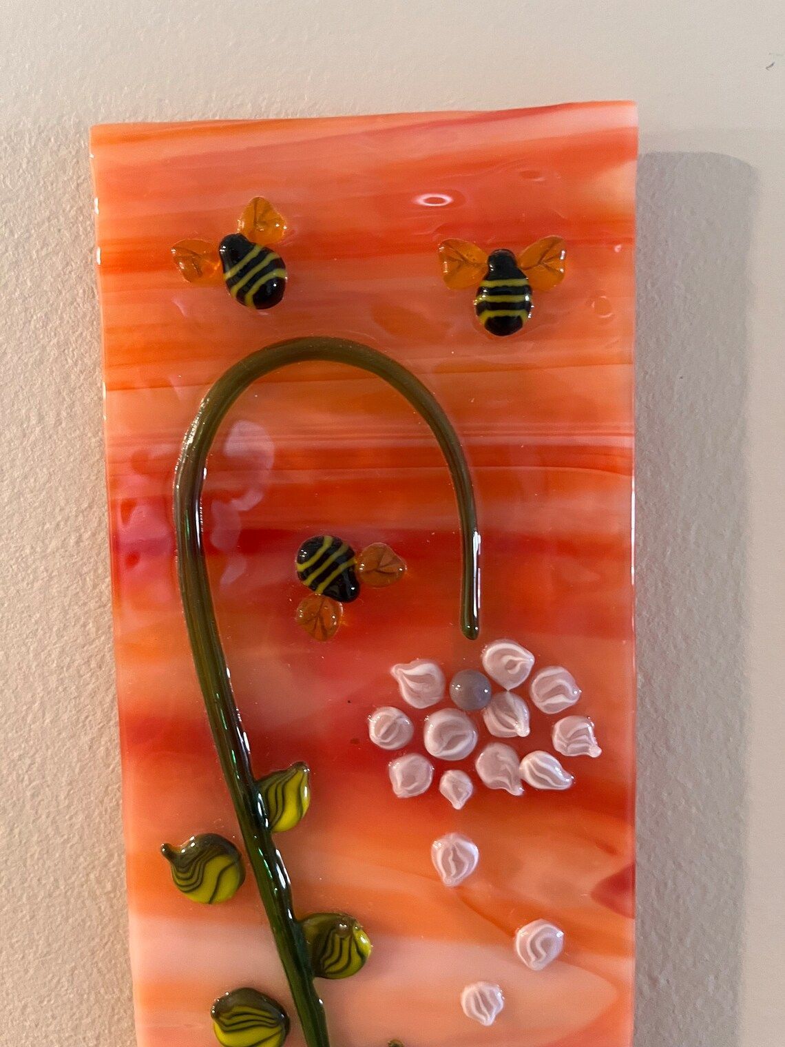 A piece of glass with bees and flowers on it is hanging on a wall.