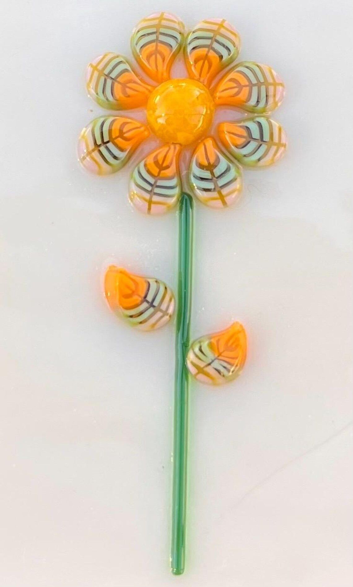 A yellow flower with green leaves is sitting on a white surface.