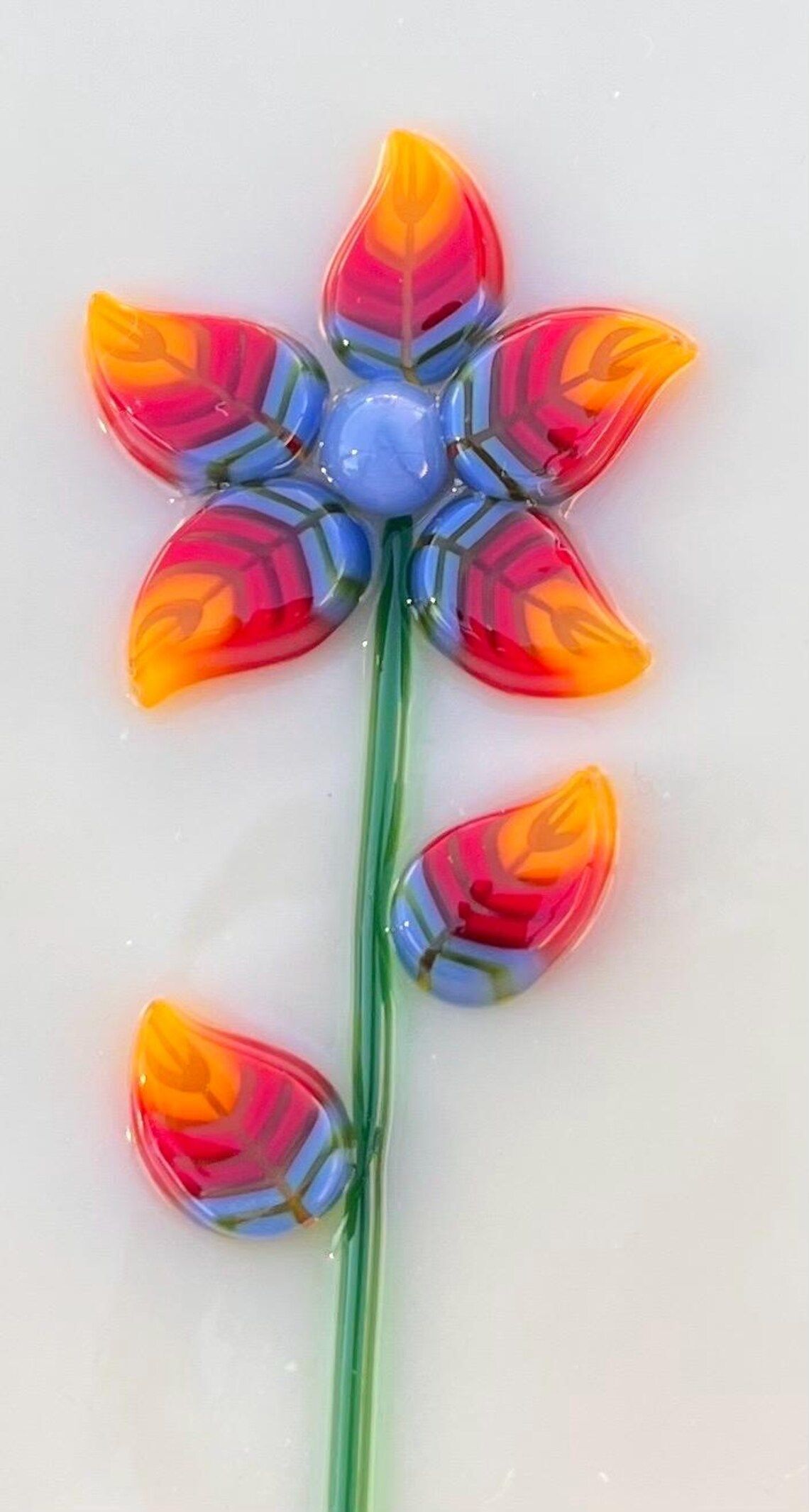 A close up of a colorful glass flower on a white surface.