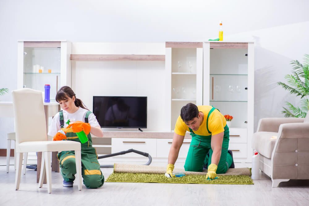 A Man and a Woman are Cleaning a Living Room With a Vacuum Cleaner — AVI Protection Group Pty Ltd in West Kempsey, NSW