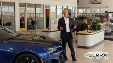 A man in a suit is standing in front of a blue car in a showroom.