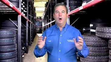 A man in a blue shirt is standing in front of a warehouse full of tires.